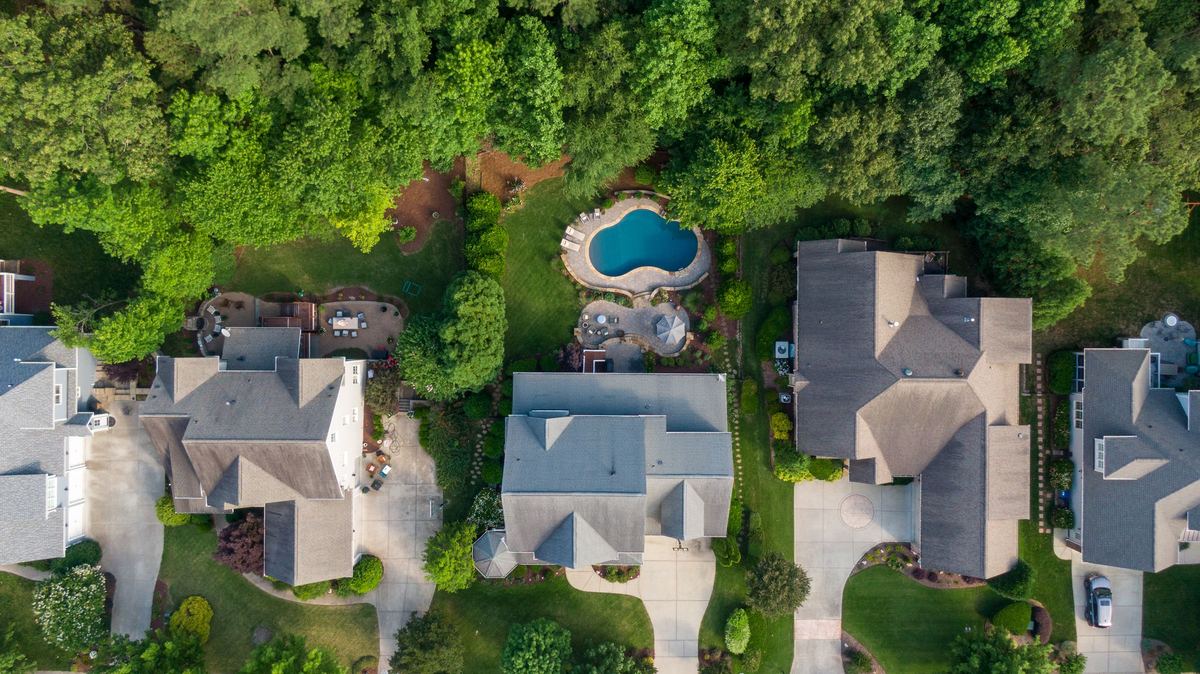 An aerial view of large suburban homes with grey roofs, a backyard pool and mature trees