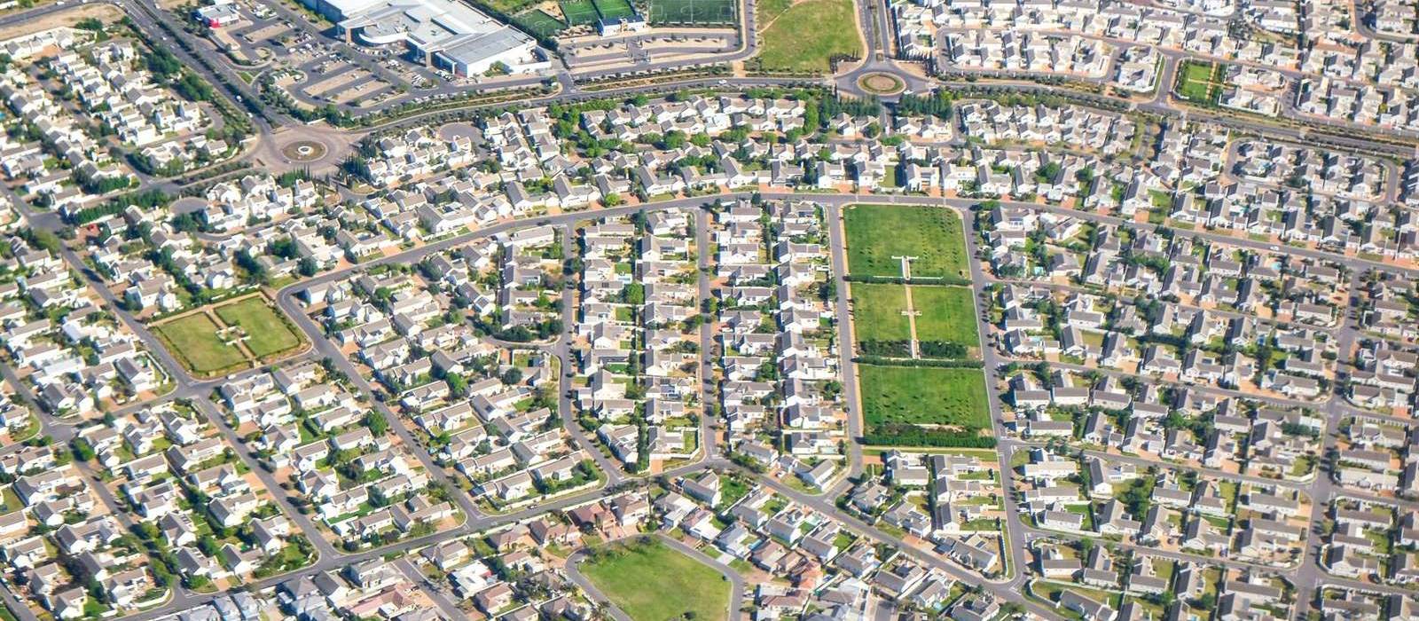A wide aerial view of a sprawling suburb, thousands of homes laid out around parks and curving streets