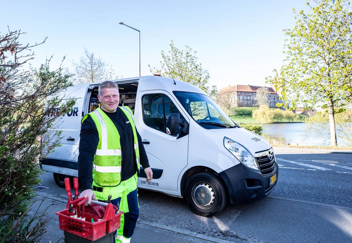 A tradesman in a high-visibility vest carrying a red toolbox beside a white work van