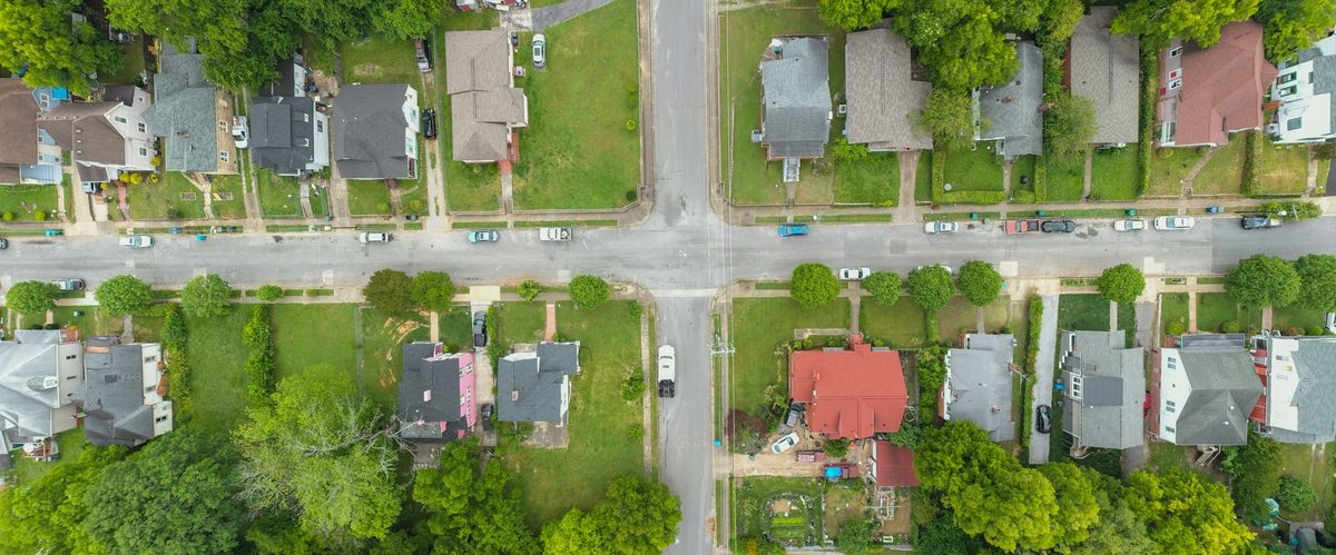 An overhead view of a suburban grid of houses, streets and green yards