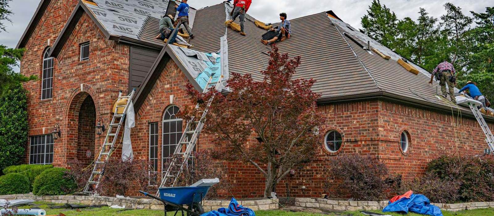 A roofing crew tearing off and replacing the shingles on a brick two-storey house